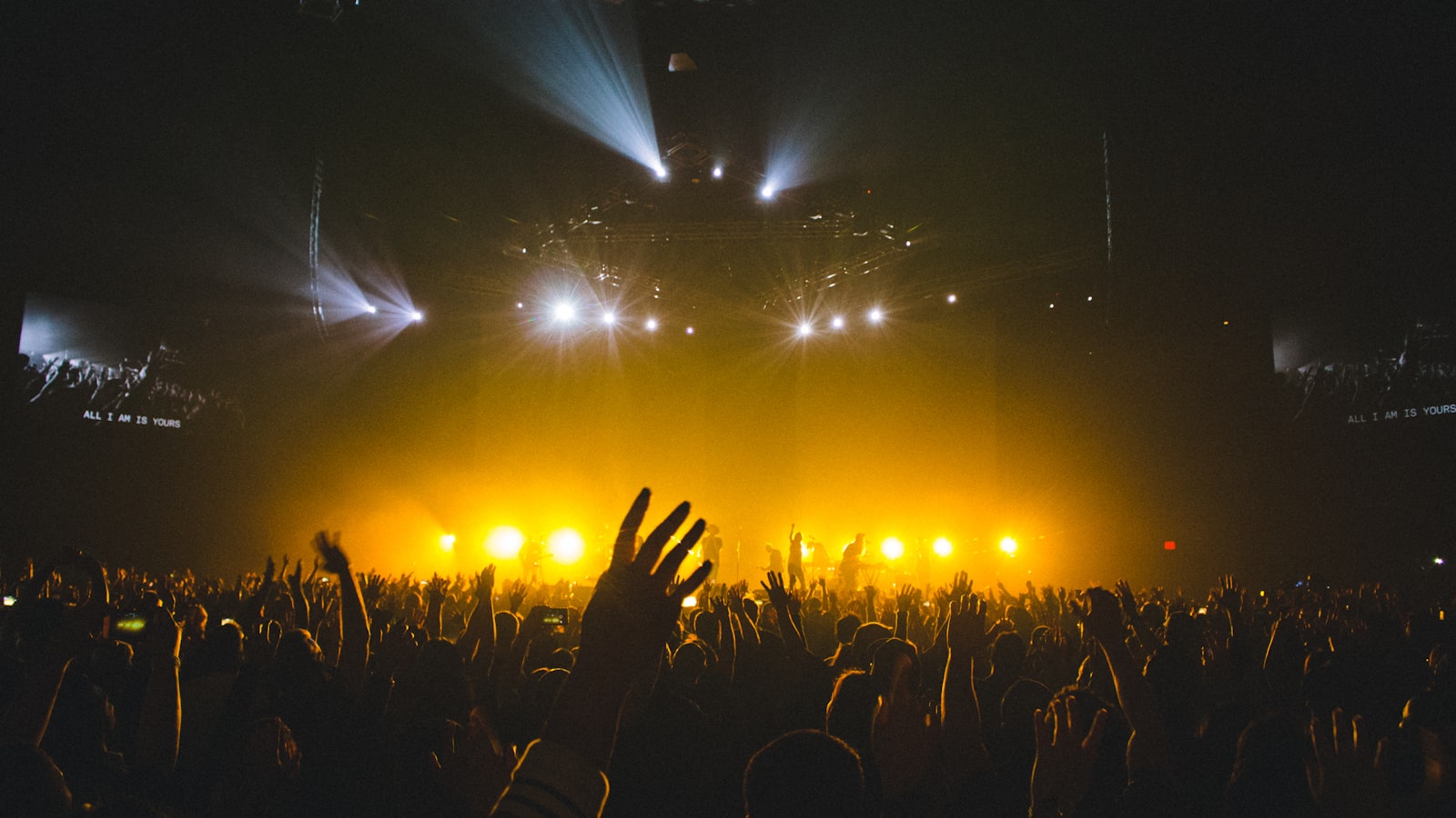 A singer stepping into a warm spotlight on stage in front of an audience