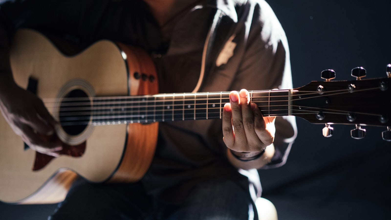 A person practicing acoustic guitar while sitting on a wooden floor.