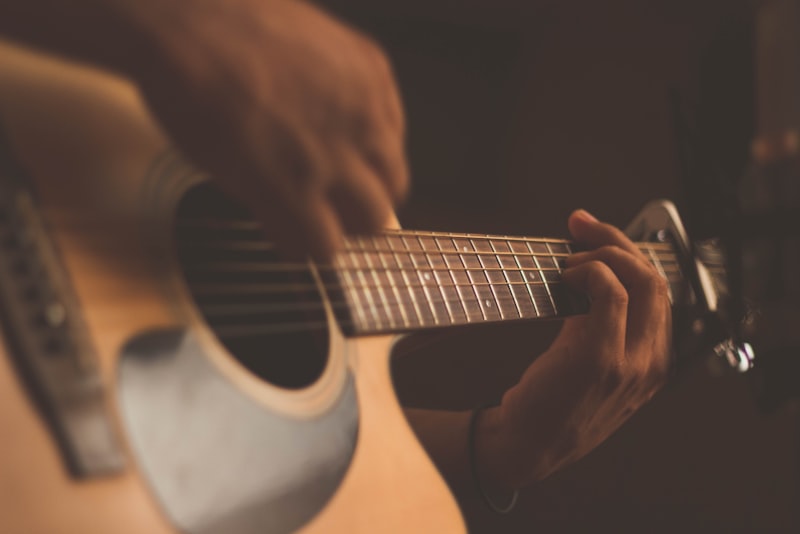 A person holding an acoustic guitar near an open window with morning light